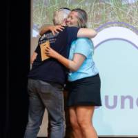 Teacher receives hug from Groundswell staff in front of projected "Groundswell" background
